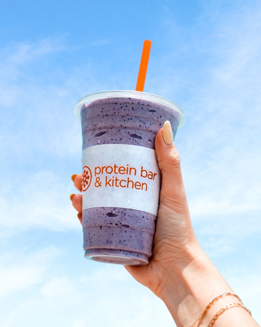 A Protein Bar & Kitchen shake or smoothie held up against a blue sky