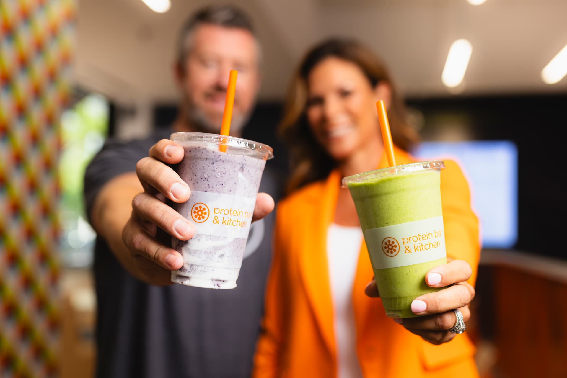 Two Protein Bar & Kitchen franchisees holding freshly blended protein shakes